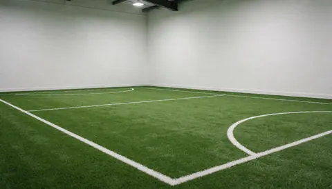 Empty indoor soccer field with white boundary lines and bright lighting, suitable for a sports club website background