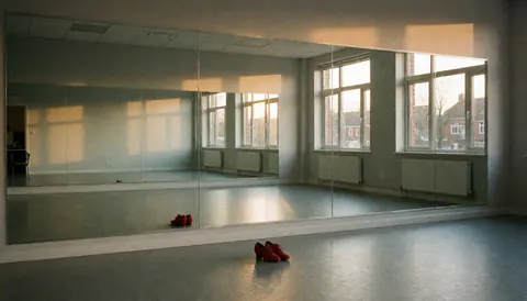 Red salsa shoes on the floor of an empty dance studio with mirrors and natural light
