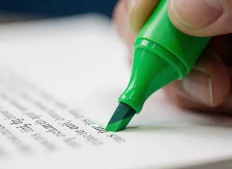Green chisel highlighter marking text on white paper with a dark blue wall background, stationery detail