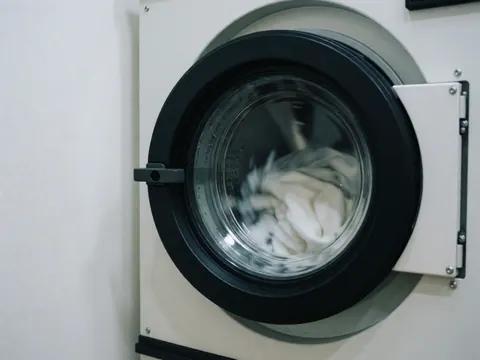 Close-up of an industrial washing machine running with white clothes and water, showing foam and condensation on a white background