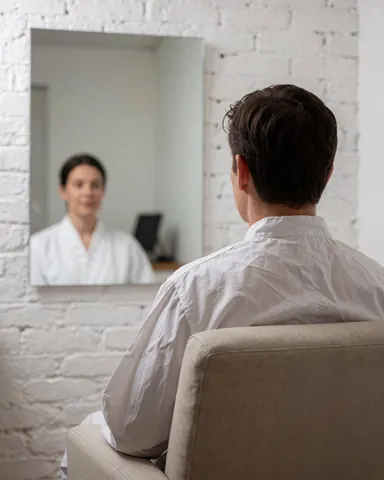 A satisfied customer sits in a chair looking at their healthy reflection in a mirror during a calm dermabrasion treatment session.