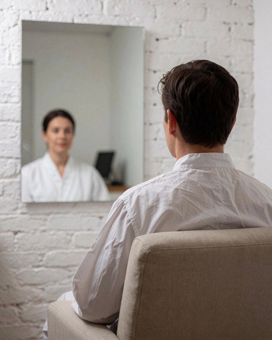A satisfied customer sits in a chair looking at their healthy reflection in a mirror during a calm dermabrasion treatment session.