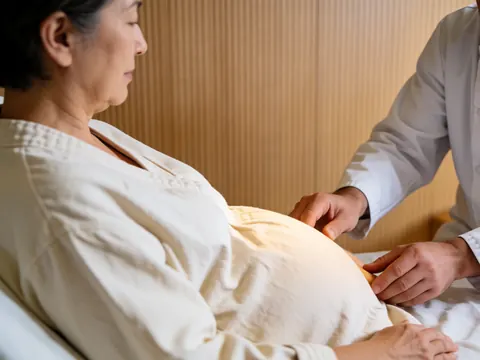 Therapist hands performing reiki massage on pregnant woman abdomen with light wood walls and warm lighting
