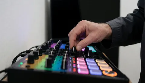 Close-up of a hand adjusting a knob on an illuminated effects unit against a white wall with party equipment visible.