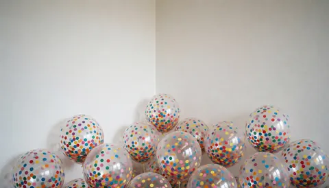 Transparent balloons filled with multicolor confetti arranged in the corner of a white room for event decoration