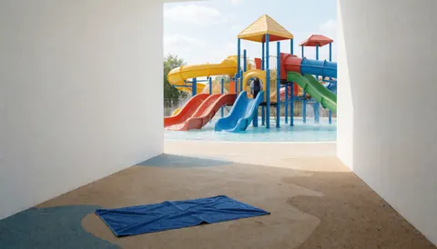 Blue towel lying on the ground in a water park slide zone with colorful slides and a person in the background
