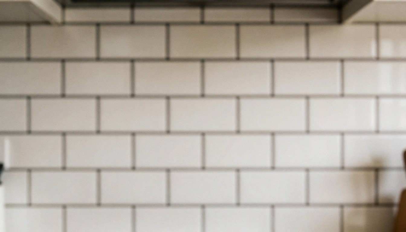 White ceramic tiles with dark grout on a kitchen wall, providing a clean and neutral background suitable for website text and design layouts.