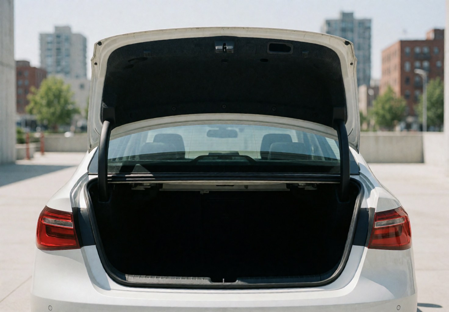 White sedan parked on urban pavement with open trunk during daylight, suitable for ride-hailing and transport services.