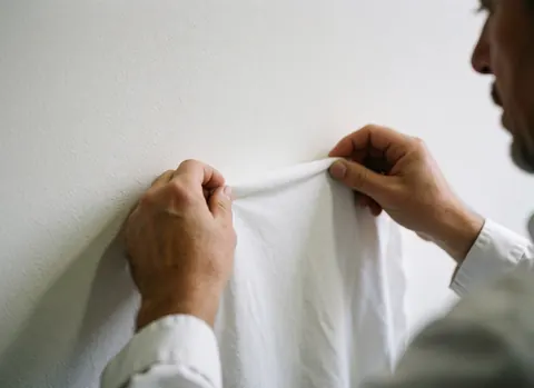 Close-up of hands checking the texture of white t-shirt material against a plain background for quality control