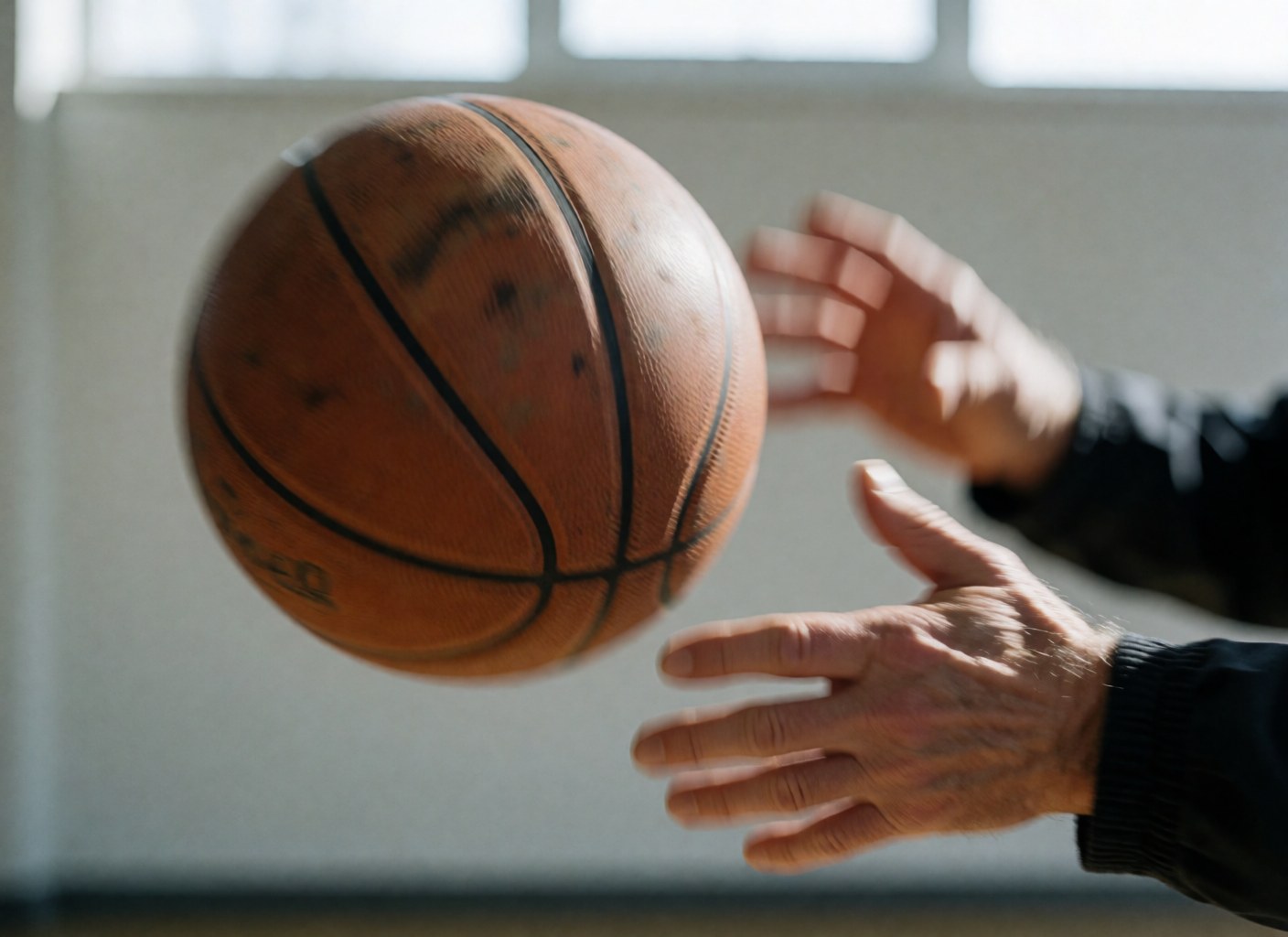 Close-up of a hand passing a basketball in a gym with bright lighting, capturing dynamic action and technique.