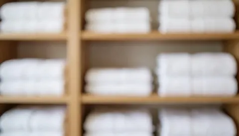 Blurred background of stacked white towels on wooden shelves, ideal for beach service text overlays