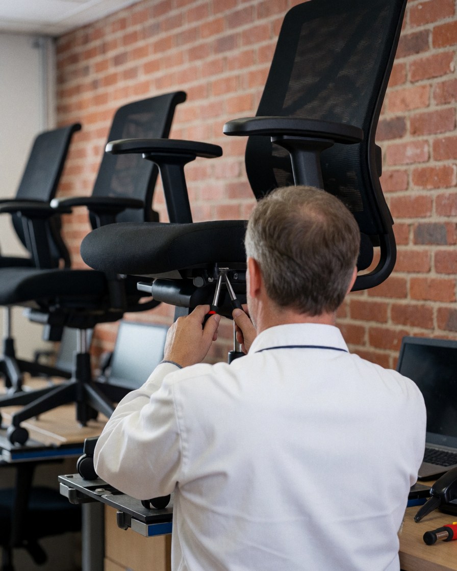 Technician repairing an office chair using a tool against a red brick wall in a professional furniture repair setting