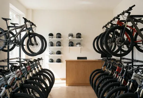 Mountain bikes hanging in a bike shop with helmets on shelves and a reception desk under natural light