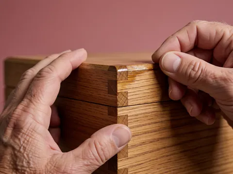 Close-up of hands applying varnish to a beveled wood joint during furniture repair
