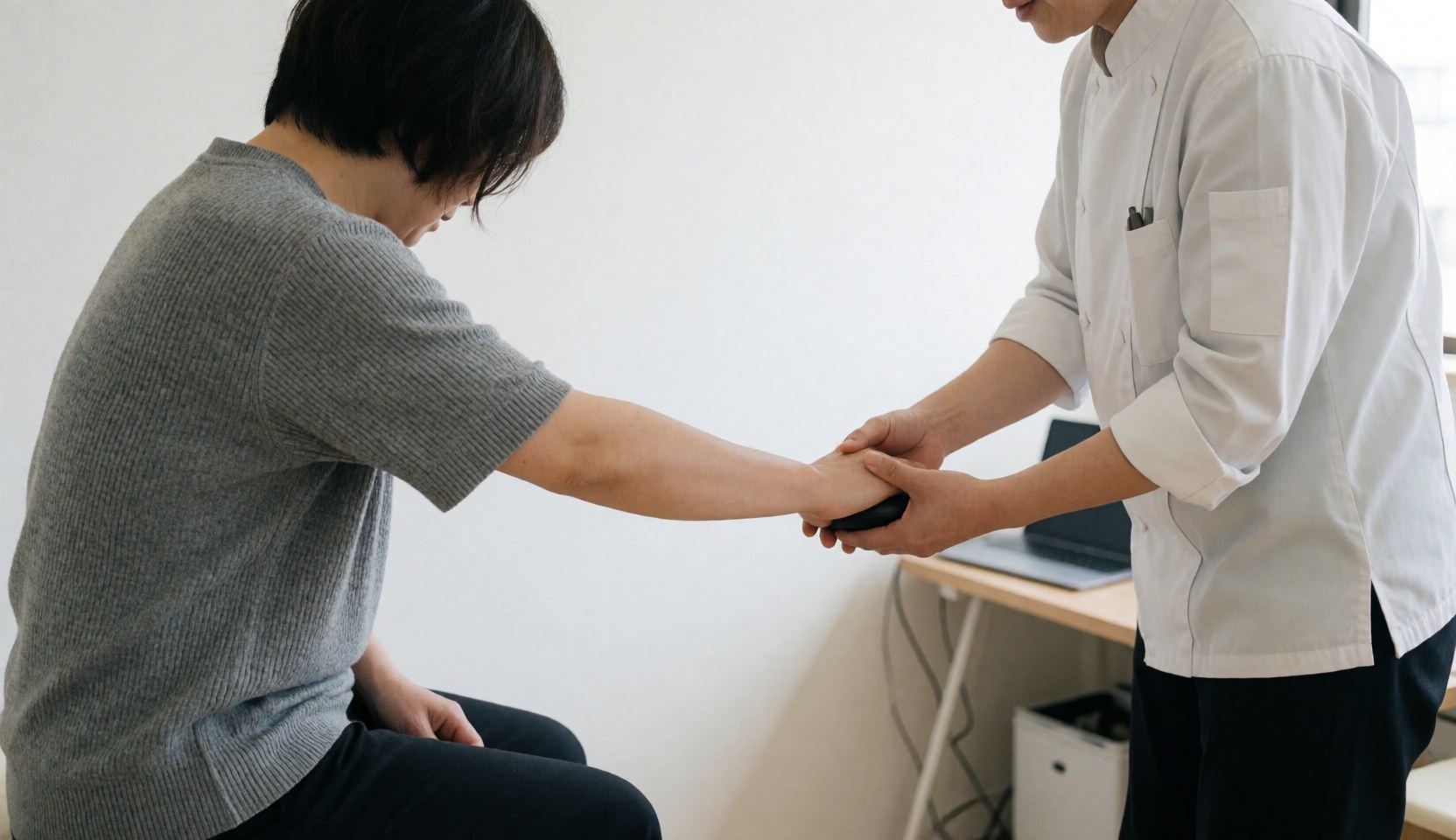 Therapist guiding client hand with massage ball in a clinic with white walls and natural light