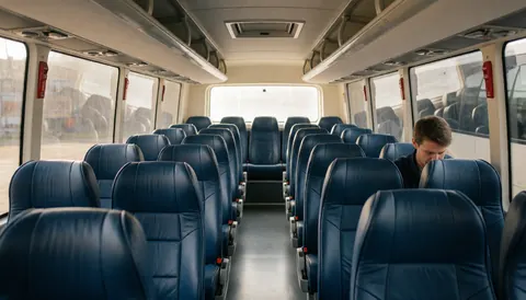 Interior view of a tour bus featuring rows of blue seats, a central aisle, and natural light streaming through large windows.