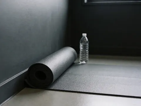 Rolled yoga mat next to water bottle in dance studio with charcoal gray walls, class tools detail