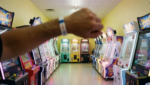 Close-up of a hand wearing a wristband in an arcade hallway with bright lights and yellow walls, suitable for a fun center website hero image