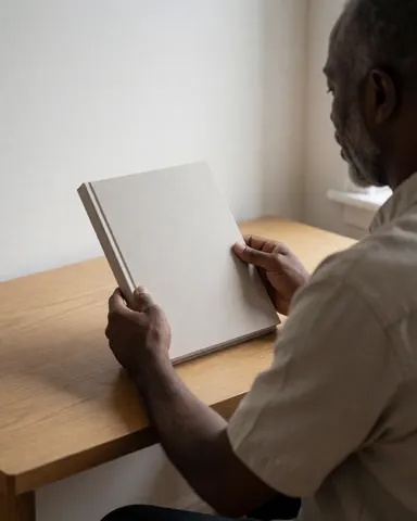 A client examines a photo book on a wooden desk in a bright office with white walls and natural light.