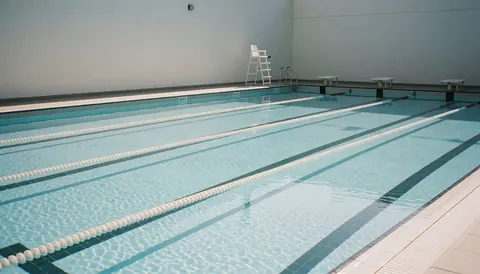 Public swimming pool with marked lanes, clear water, and a lifeguard chair on the edge, suitable for website hero section