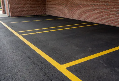 Empty parking lot with yellow painted lines on black asphalt adjacent to a red brick wall, ready for vehicles.