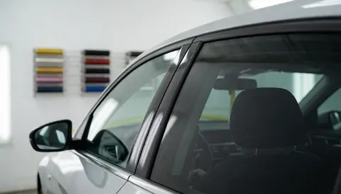 A car with tinted windows inside a glass tinting workshop with film samples visible in the background against white walls