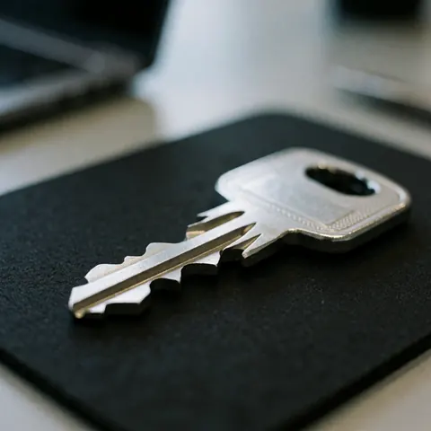 Close-up of a high-security metal key with embossed details resting on a matte black surface, suitable for locksmith business marketing.