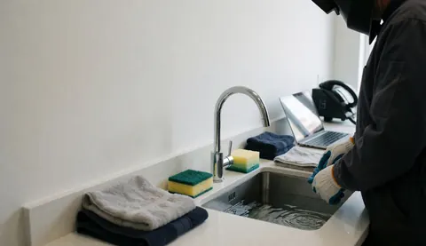 A person wearing gloves cleans underwater photography gear using towels and sponges in a sink area.