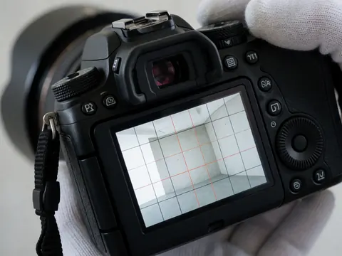 Close-up of a professional camera displaying a leveling grid on its LCD screen, with a gloved hand adjusting the dial against a smooth concrete background.