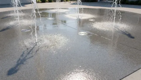 Water park background with water sprays splashing on wet concrete floor and circular drains, ideal for website hero section