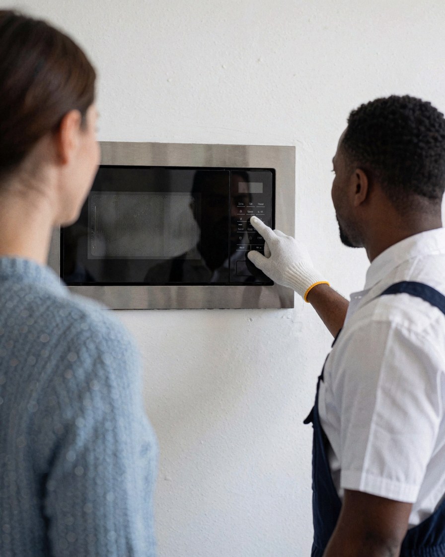 Technician testing a newly installed built-in microwave oven against a white wall.