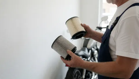 Close-up of a mechanic holding a new and a used air filter side by side for comparison during a motorcycle service.