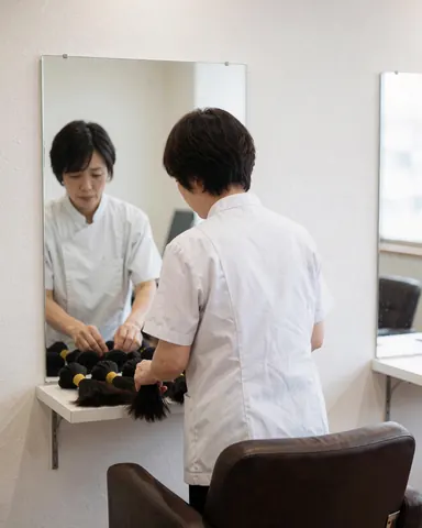 A stylist organizes hair extensions on a shelf in a professional salon with a mirror and chair.