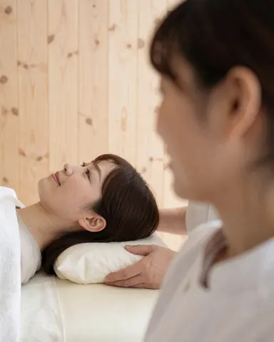 Therapist performing deep neck massage on a client lying on a table with light wood walls in a professional setting