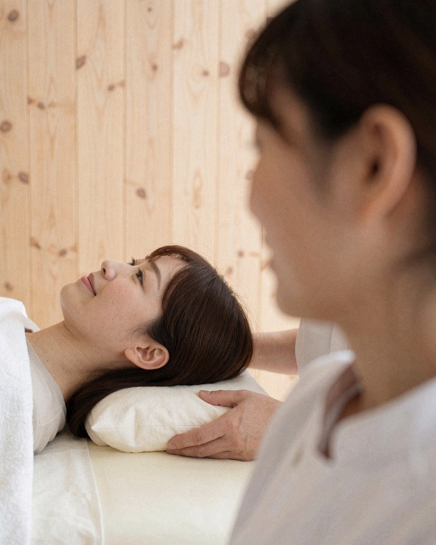 Therapist performing deep neck massage on a client lying on a table with light wood walls in a professional setting