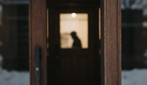 Dark wooden door frame with warm light inside and snow outside, suitable as a text background for mountain hut imagery