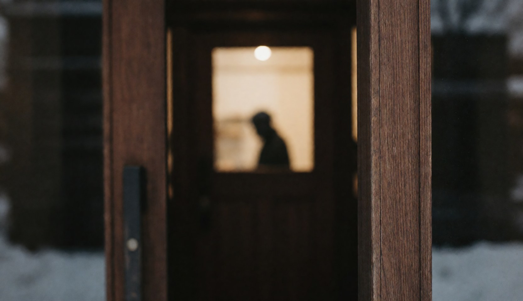 Dark wooden door frame with warm light inside and snow outside, suitable as a text background for mountain hut imagery