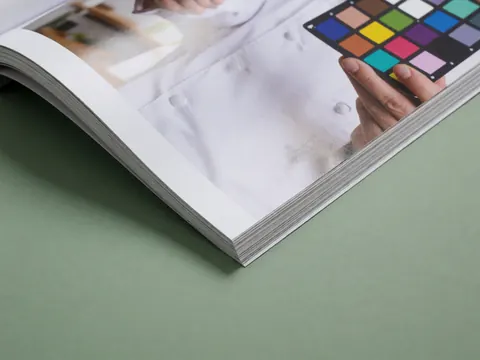 An open magazine featuring a color checker chart, glossy paper, and a green background, useful for product photographers.