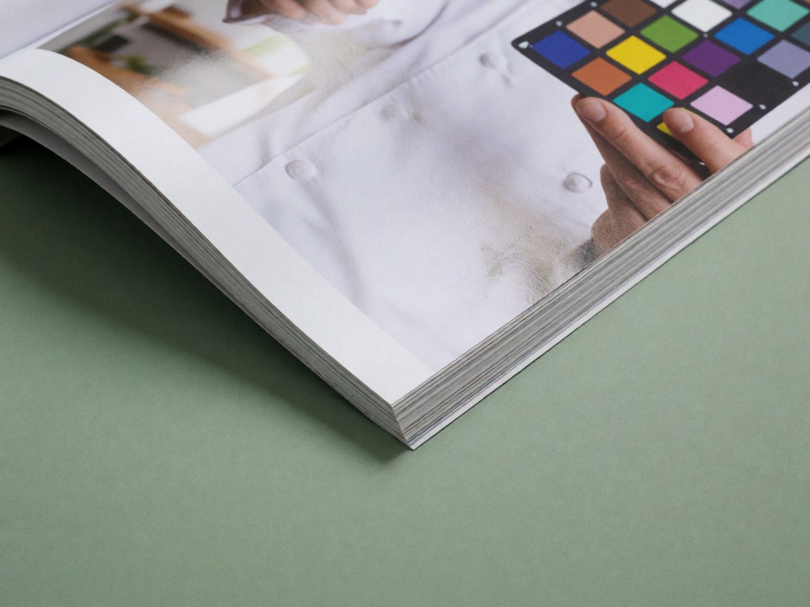 An open magazine featuring a color checker chart, glossy paper, and a green background, useful for product photographers.