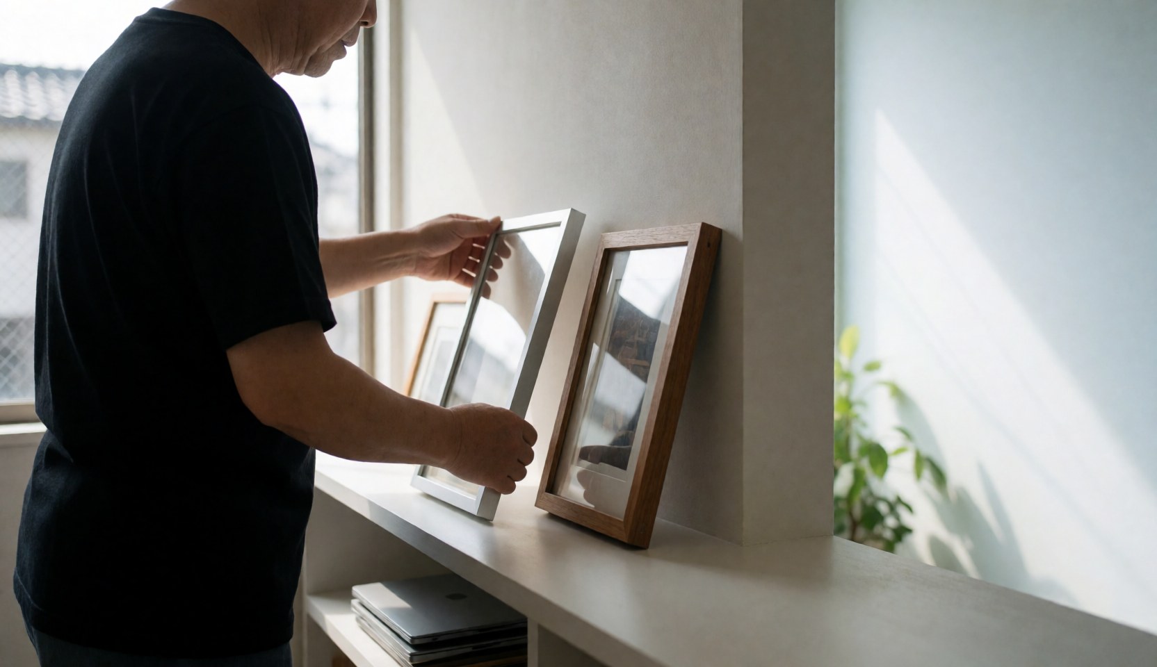 Wedding photographer organizing silver and wooden photo frames on a white shelf with natural light and copy space.