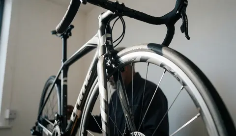 Close-up of a carbon frame road bicycle inside a bike repair shop with a mechanic working in the background.