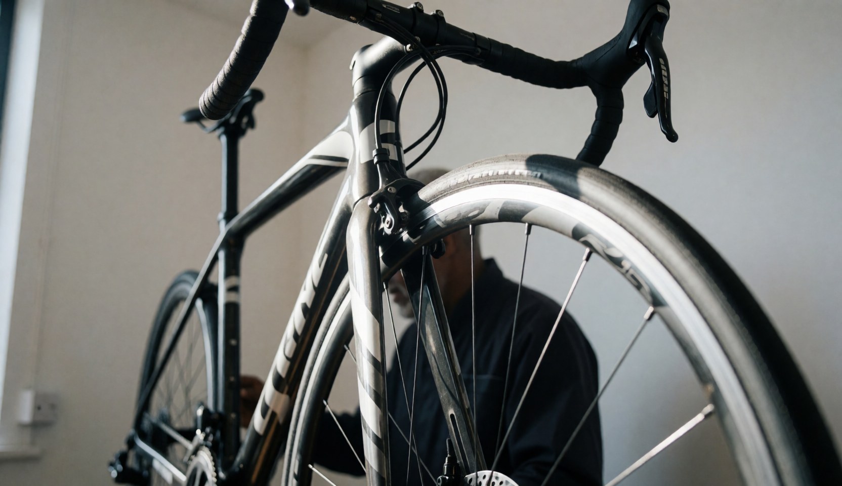 Close-up of a carbon frame road bicycle inside a bike repair shop with a mechanic working in the background.