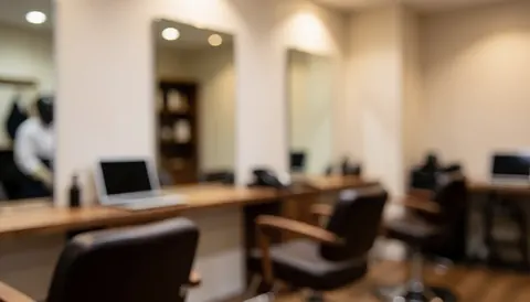 Softly blurred interior of a hair salon featuring styling chairs, wall mirrors, and work tables, providing a clean backdrop for text or business headers.