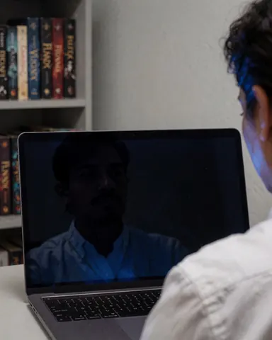 Person using laptop with fantasy books on shelf, creative writing scene in office.
