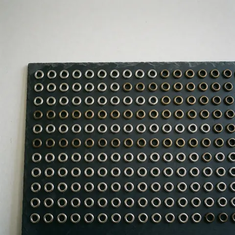 Rows of silver and antique bronze metal grommets arranged neatly on a dark slate surface for textile or leather industry use