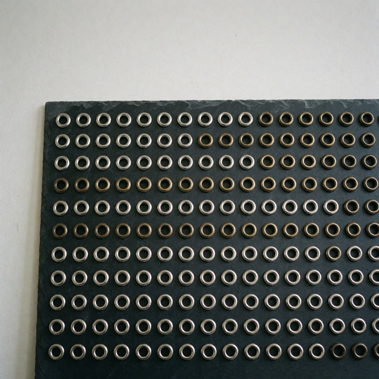 Rows of silver and antique bronze metal grommets arranged neatly on a dark slate surface for textile or leather industry use