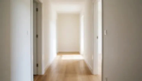 An empty hallway featuring wooden flooring and white walls, illuminated by natural light at the end, providing a clean background for business text.