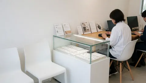 Glass jewelry display case in a modern piercing studio with white chairs and staff working at computers