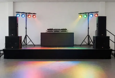 Empty party stage setup featuring DJ tables, speakers, and colorful lighting ready for an event.