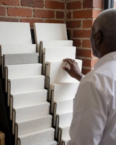 A customer examines various textured papers displayed on a shelf in a stationery store with a red brick wall background.